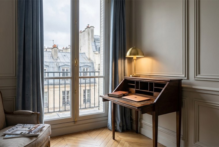 Coin bureau d'un appartement haussmannien Worknest — bureau ancien devant une fenêtre sur les toits de Paris